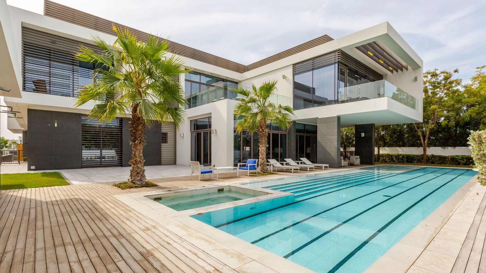 Casa contemporánea de dos pisos con piscina larga, terraza de madera y palmeras